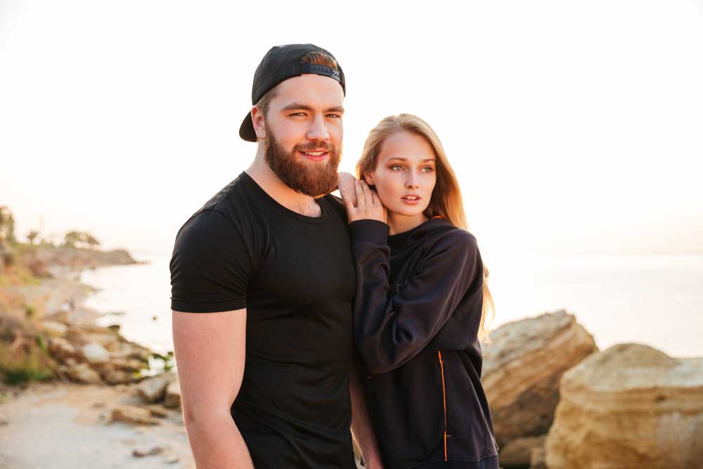 young couple standing on cliffside overlooking sunset